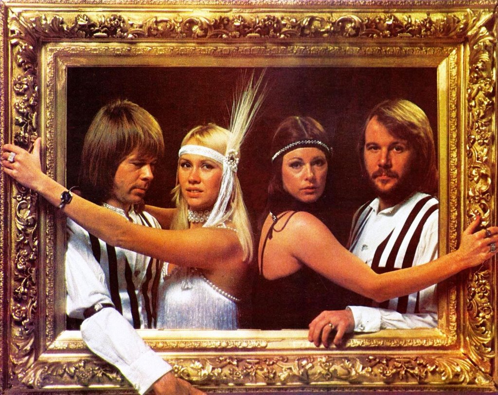 All four members of ABBA standing inside a large gold picture frame wearing 1930s black and white outfits